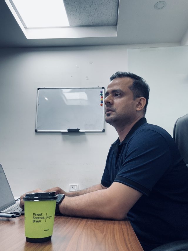 Mahabir working at his office desk on a Saturday with a coffee, laptop, and a blank whiteboard behind him